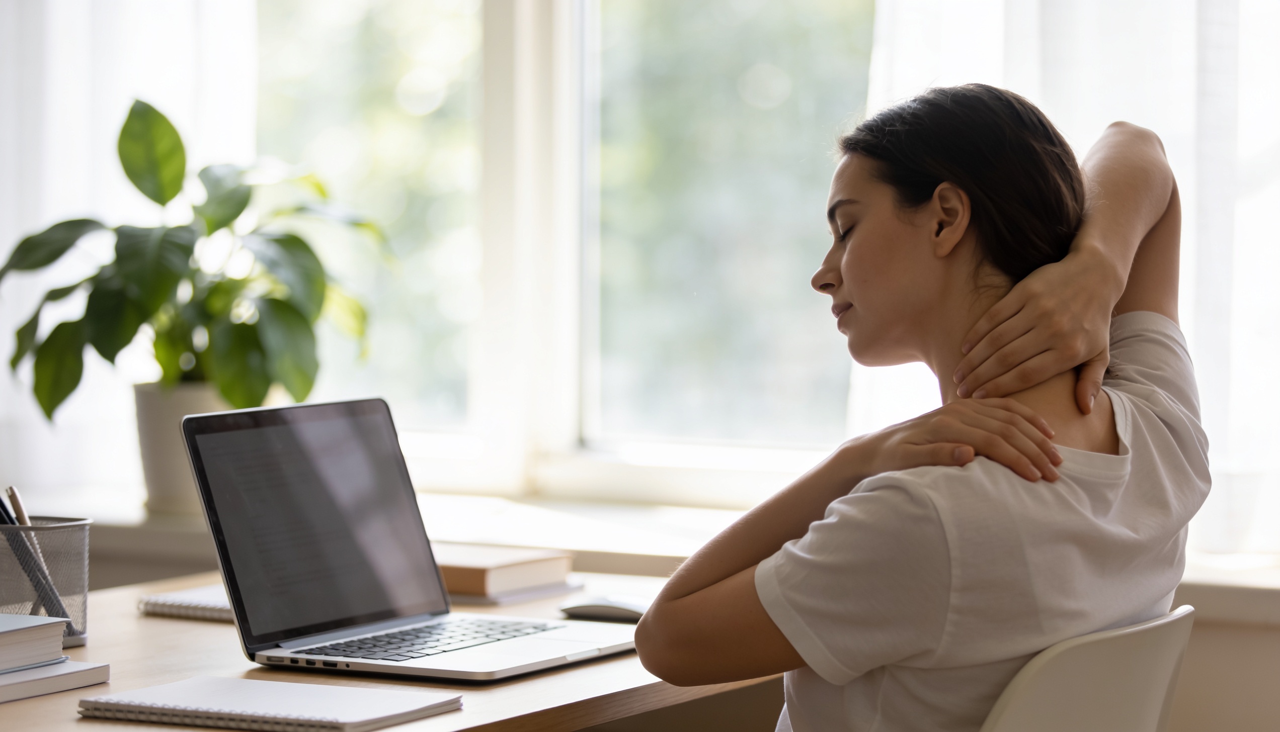 A person doing a gentle neck and shoulder stretch at a sunny desk