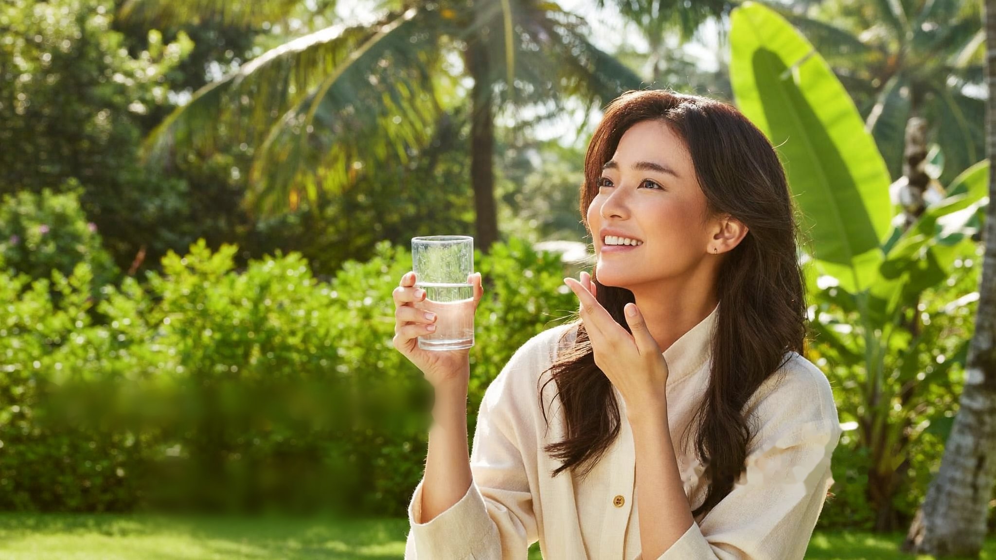 A woman enjoying a calm moment with a glass of water in a bright sage-green kitchen